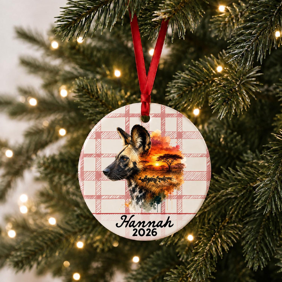 Personalized african wild dog ceramic ornament with name and year on red plaid hanging on a lit Christmas tree