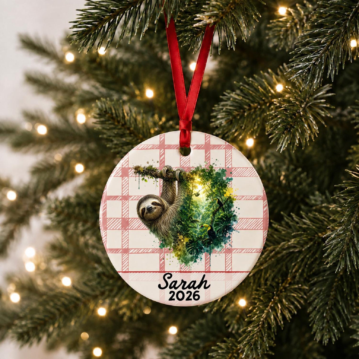 Personalized sloth ceramic ornament with name and year on red plaid hanging on a lit Christmas tree