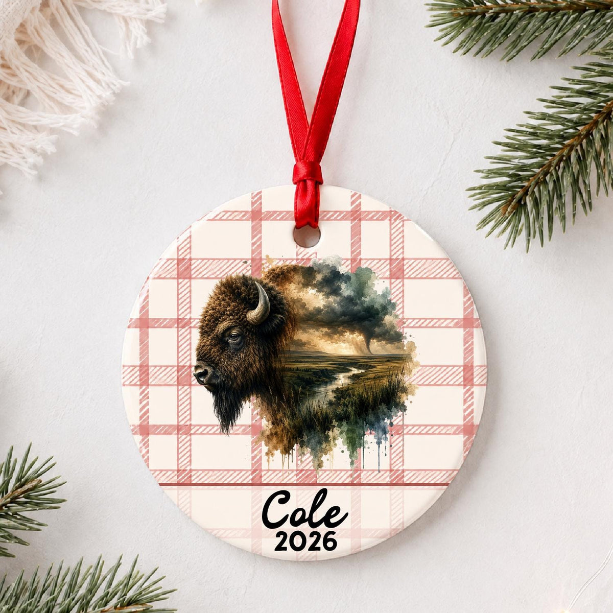 Personalized american bison ceramic ornament with name and year on red plaid styled with pine branches on a soft white background