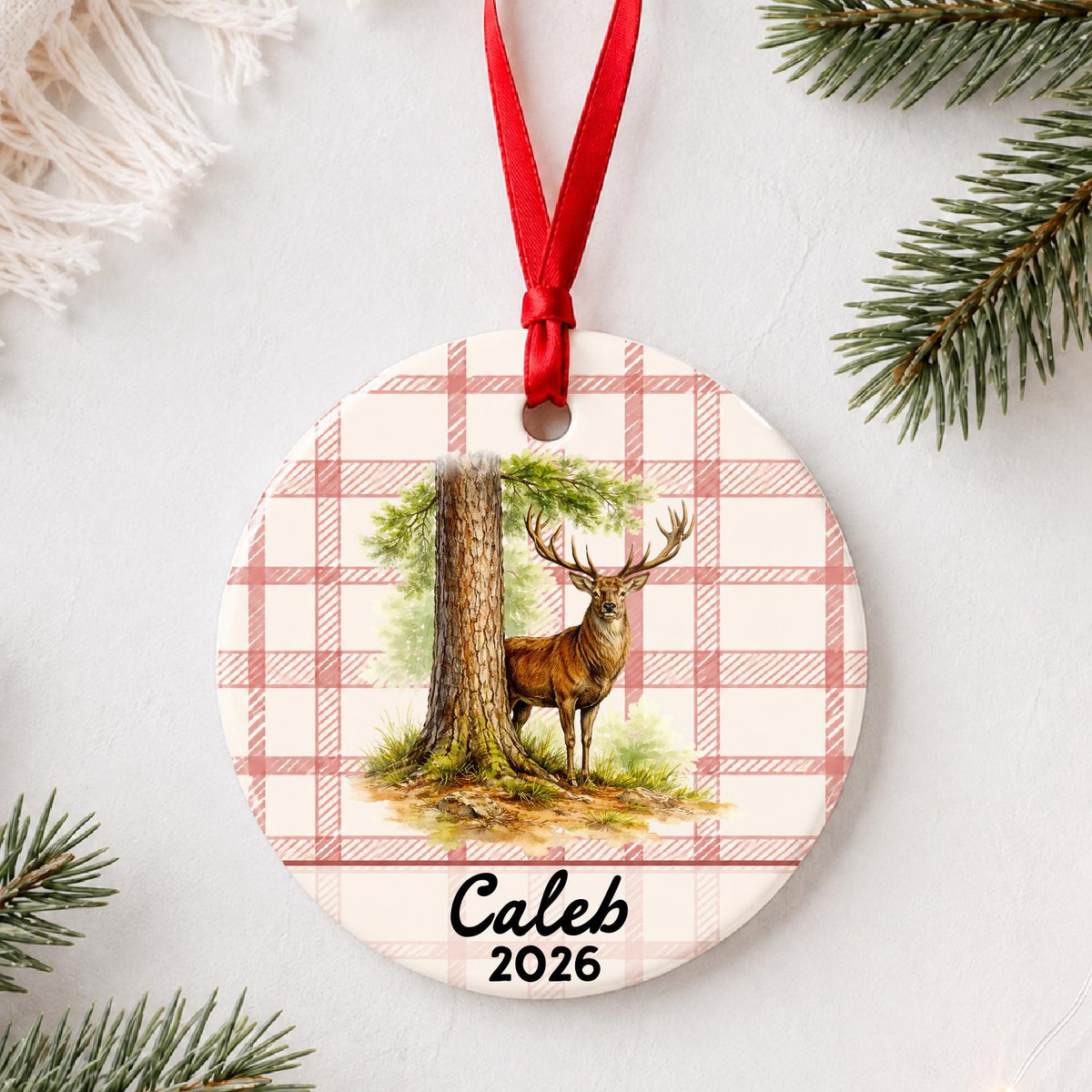 Personalized red deer stag ceramic ornament with name and year on red plaid styled with pine branches on a soft white background