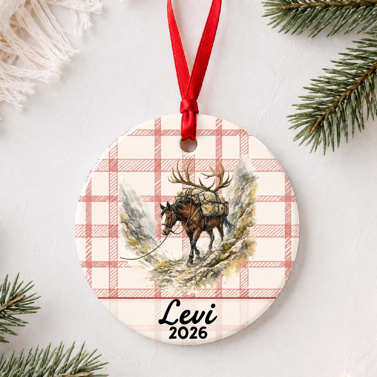 Personalized pack horse ceramic ornament with name and year on red plaid styled with pine branches on a soft white background