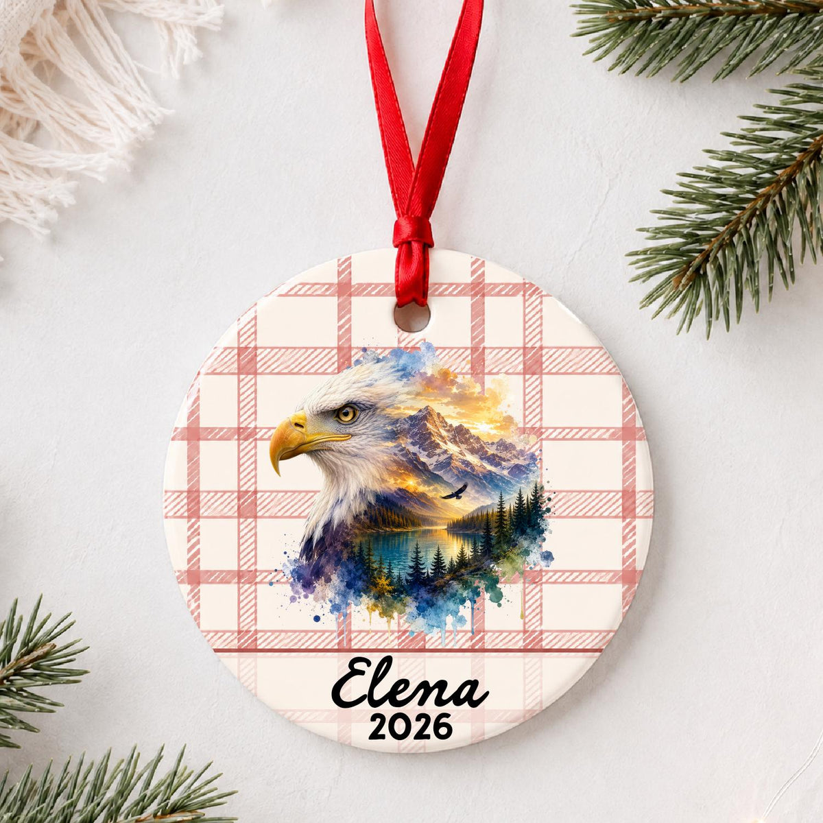 Personalized bald eagle ceramic ornament with name and year on red plaid styled with pine branches on a soft white background