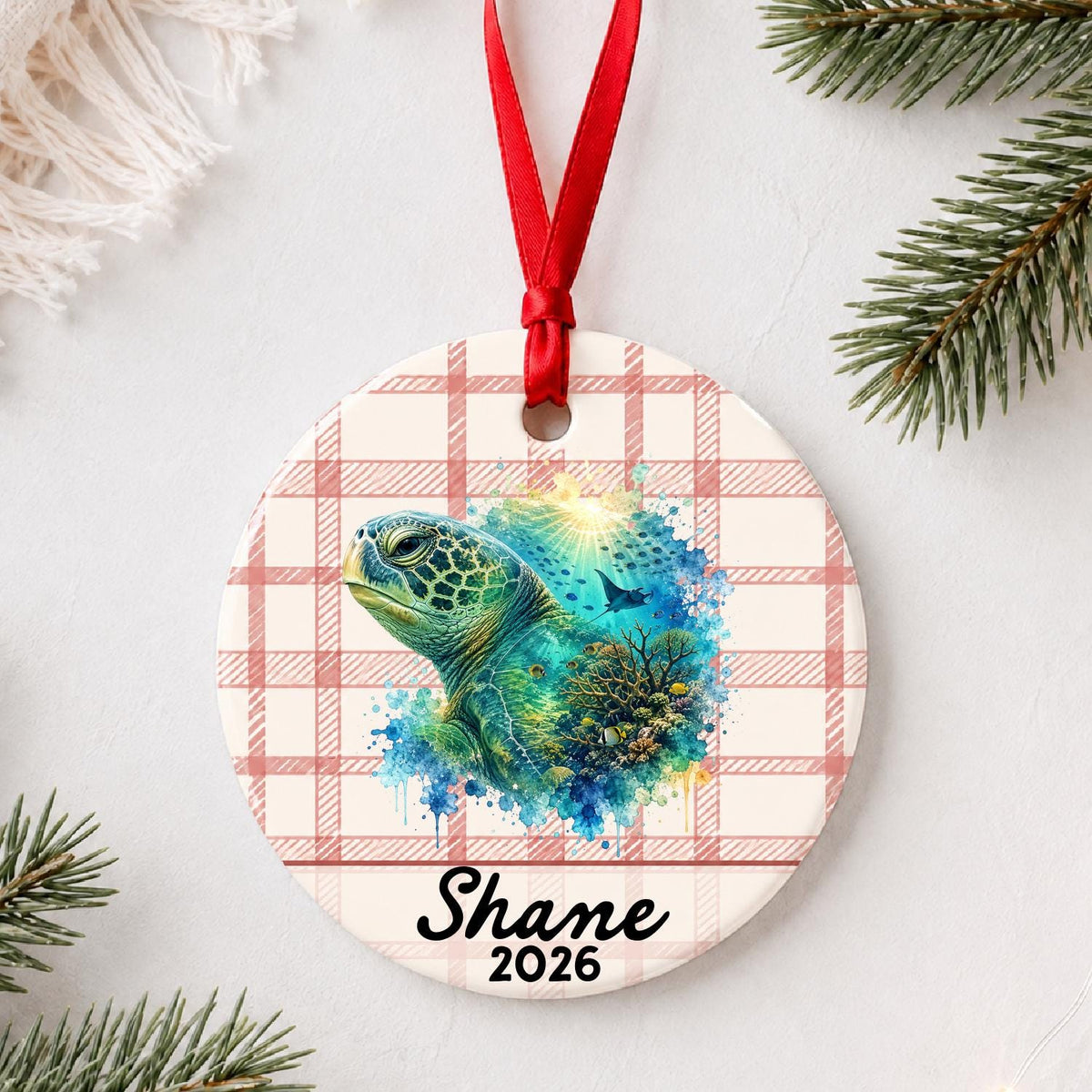 Personalized green sea turtle ceramic ornament with name and year on red plaid styled with pine branches on a soft white background