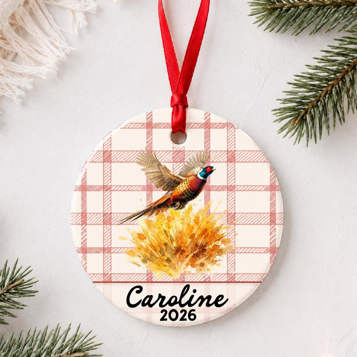 Personalized ring-necked pheasant ceramic ornament with name and year on red plaid styled with pine branches on a soft white background