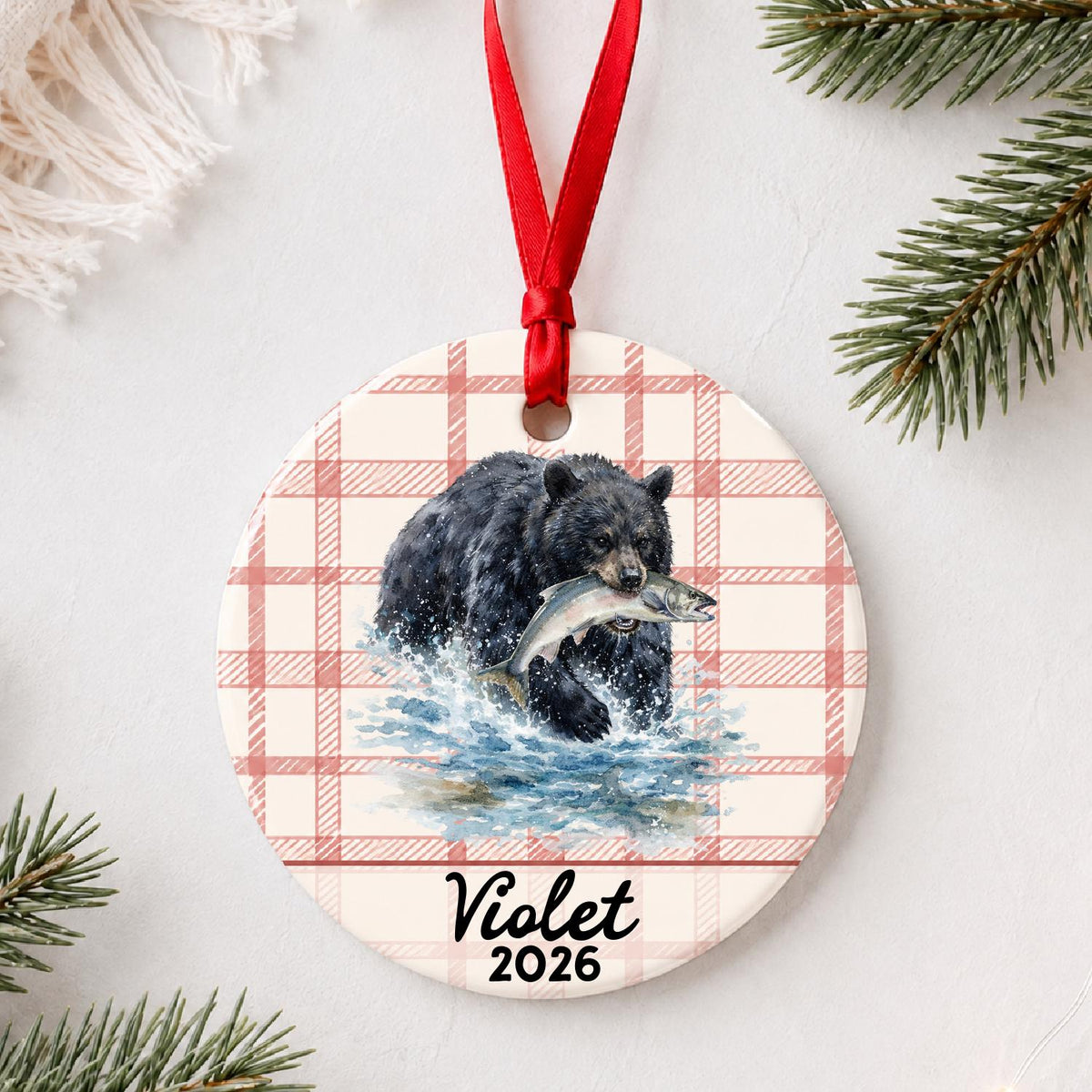 Personalized American black bear ceramic ornament with name and year on red plaid styled with pine branches on a soft white background