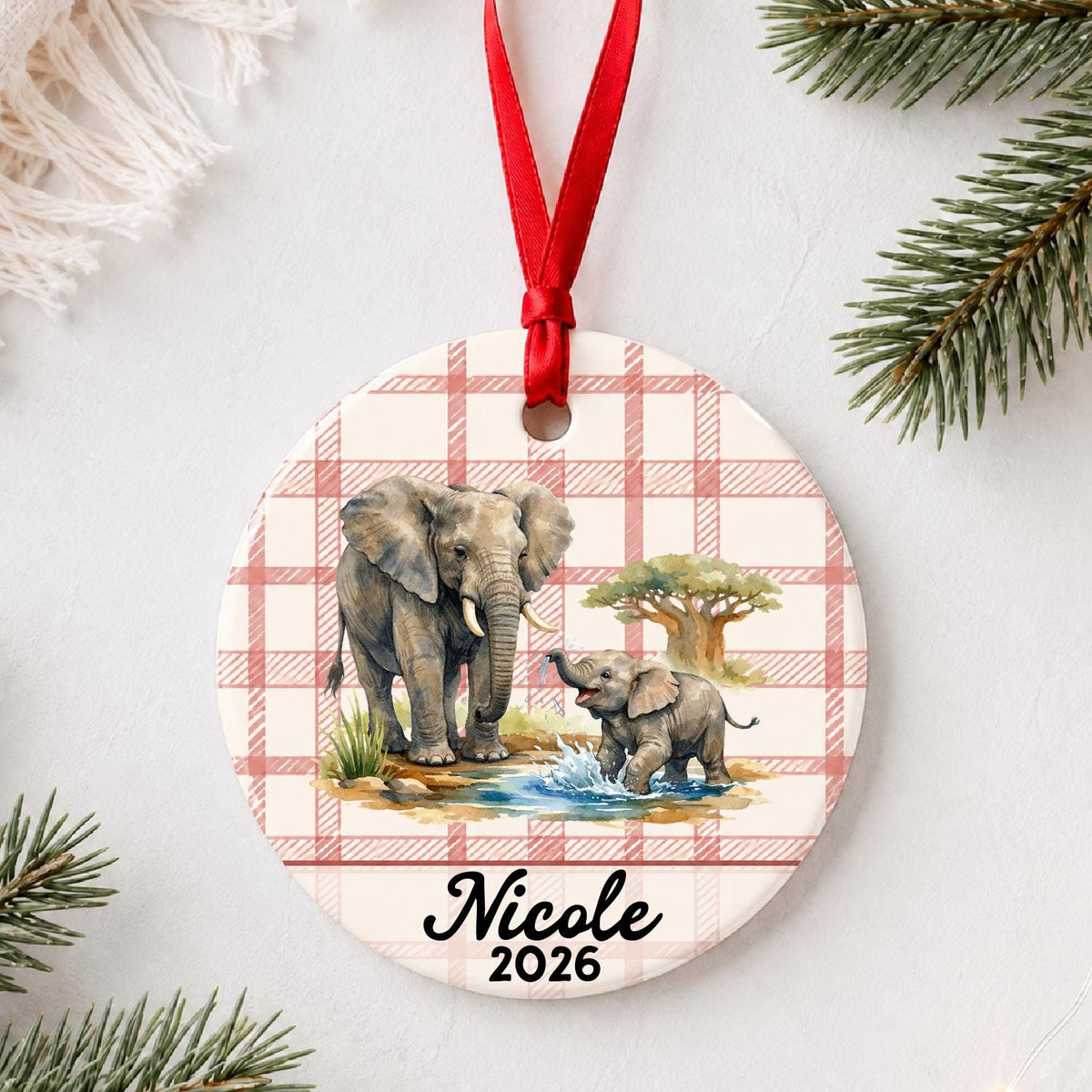 Personalized African elephant ceramic ornament with name and year on red plaid styled with pine branches on a soft white background