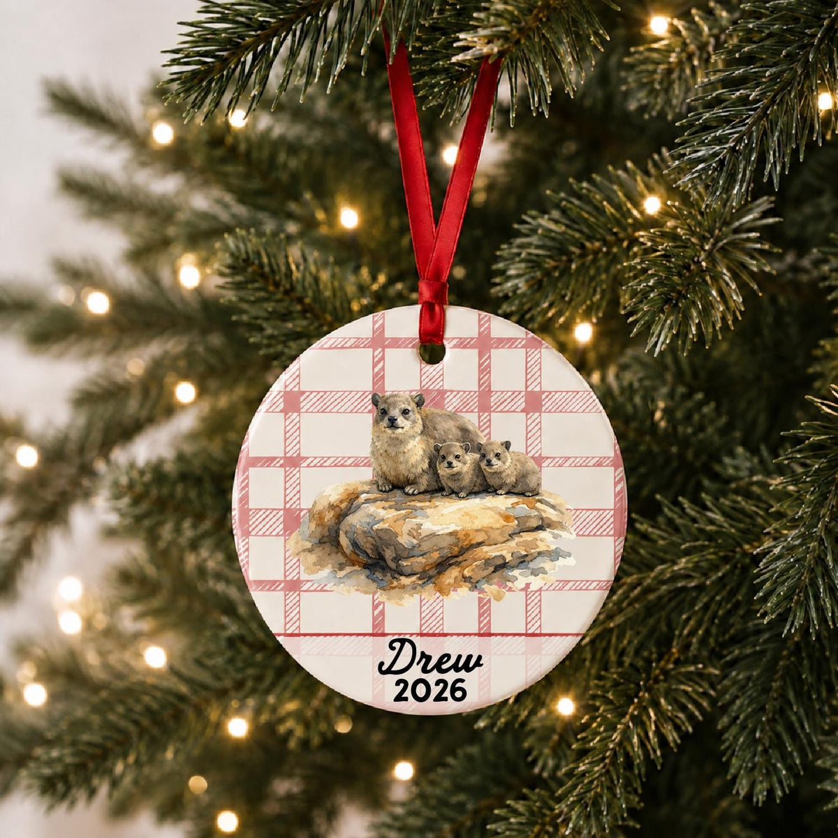 Personalized rock hyraxes ceramic ornament with name and year on red plaid hanging on a lit Christmas tree