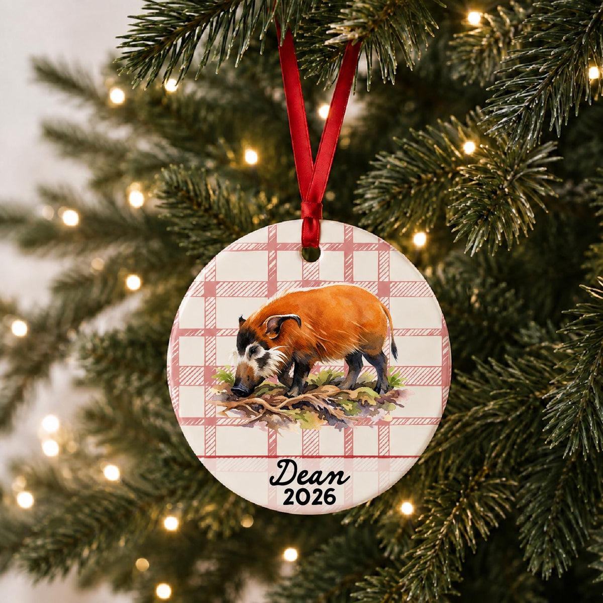 Personalized red river hog ceramic ornament with name and year on red plaid hanging on a lit Christmas tree