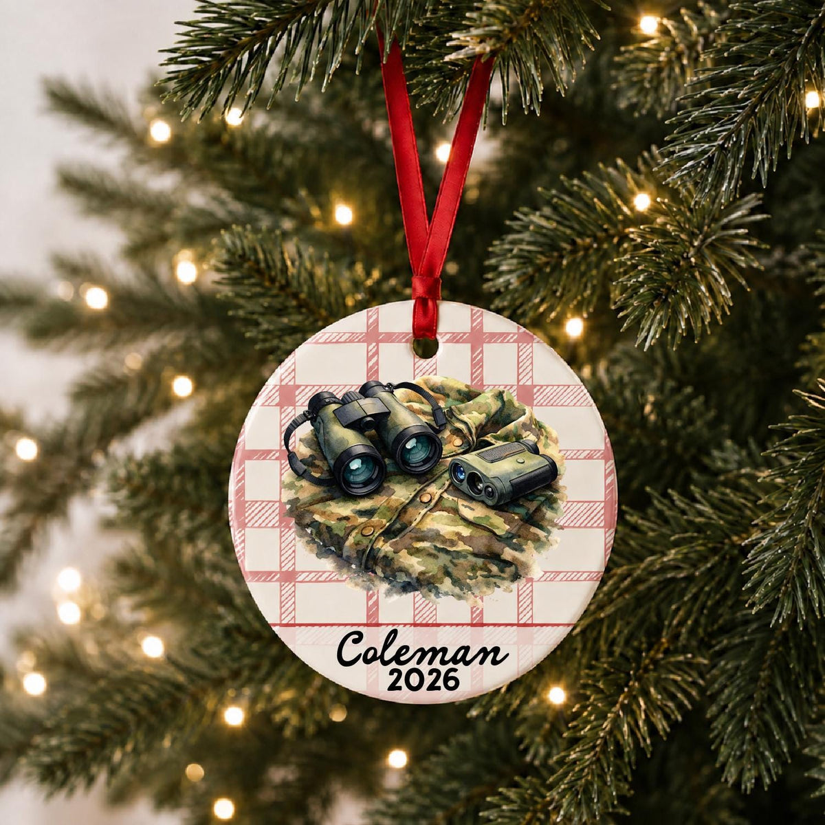 Personalized binoculars and rangefinder ceramic ornament with name and year on red plaid hanging on a lit Christmas tree