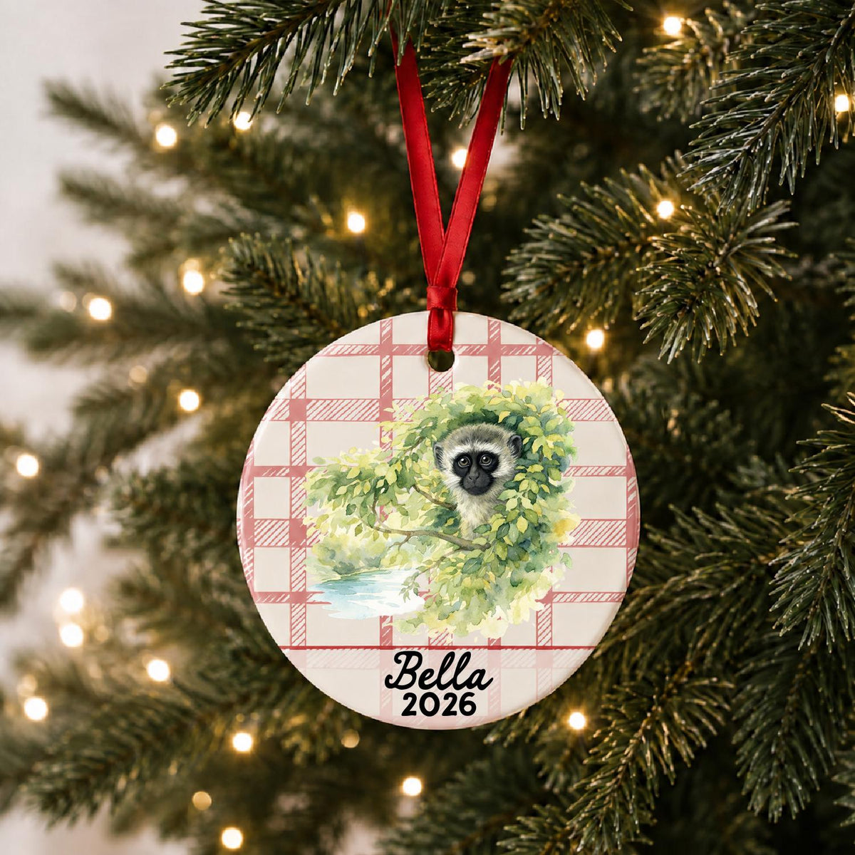 Personalized vervet monkey ceramic ornament with name and year on red plaid hanging on a lit Christmas tree