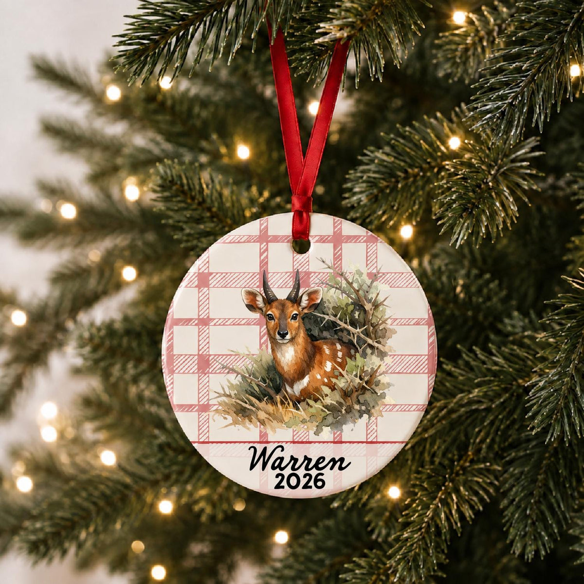 Personalized bushbuck ceramic ornament with name and year on red plaid hanging on a lit Christmas tree