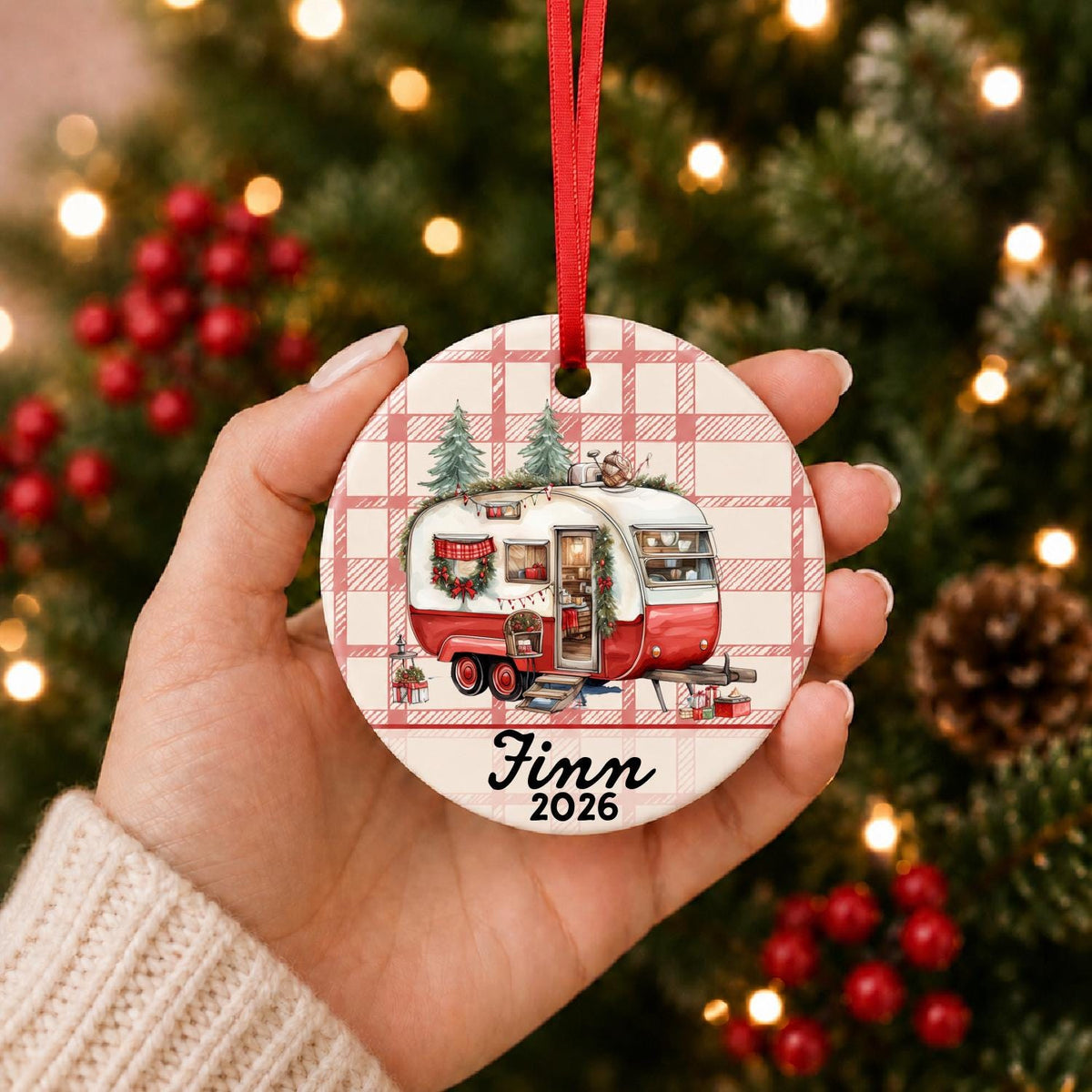 Hand holding personalized vintage camper ceramic Christmas ornament with red ribbon, name and year
