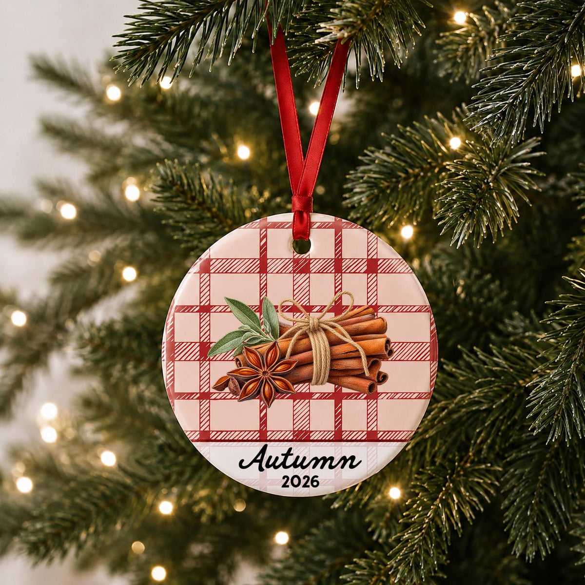 Personalized cinnamon stick ceramic ornament with name and year on red plaid hanging on a lit Christmas tree
