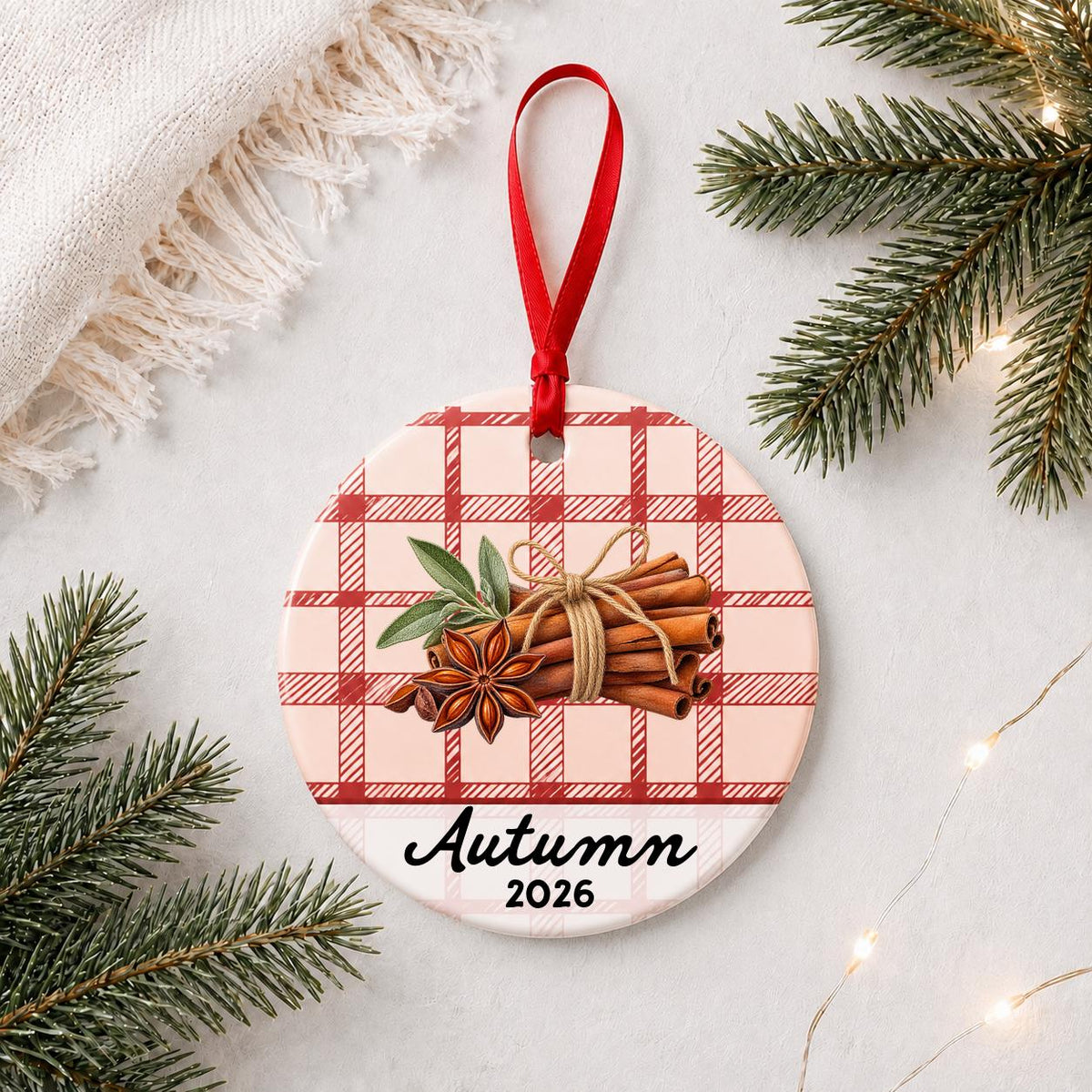 Personalized cinnamon stick ceramic ornament with name and year on red plaid styled with pine branches on a soft white background
