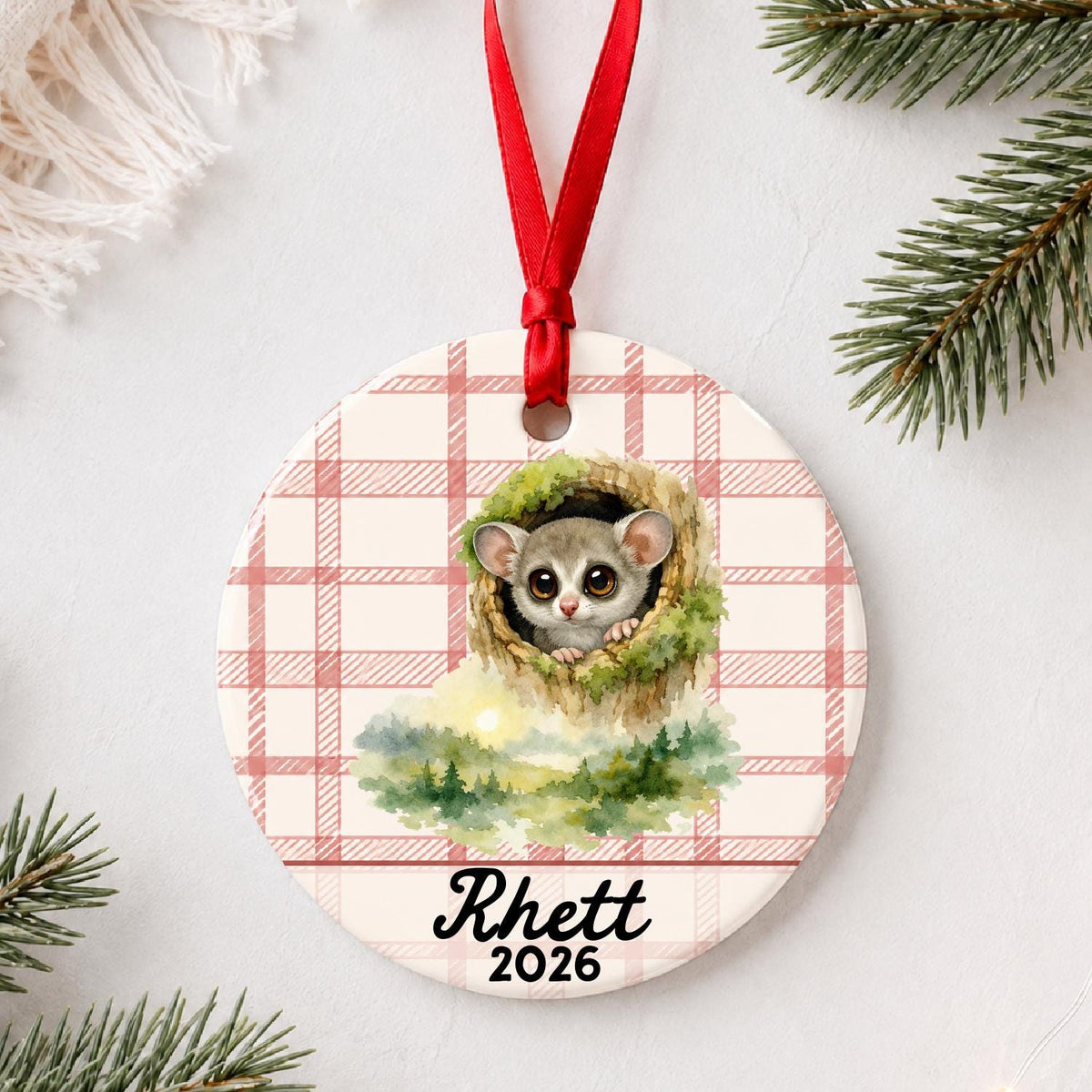 Personalized galago ceramic ornament with name and year on red plaid styled with pine branches on a soft white background