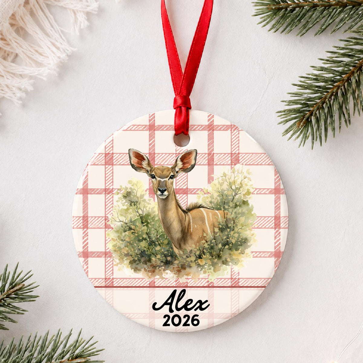 Personalized kudu in woodland ceramic ornament with name and year on red plaid styled with pine branches on a soft white background
