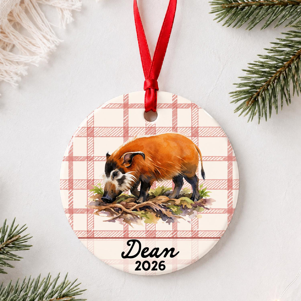 Personalized red river hog ceramic ornament with name and year on red plaid styled with pine branches on a soft white background
