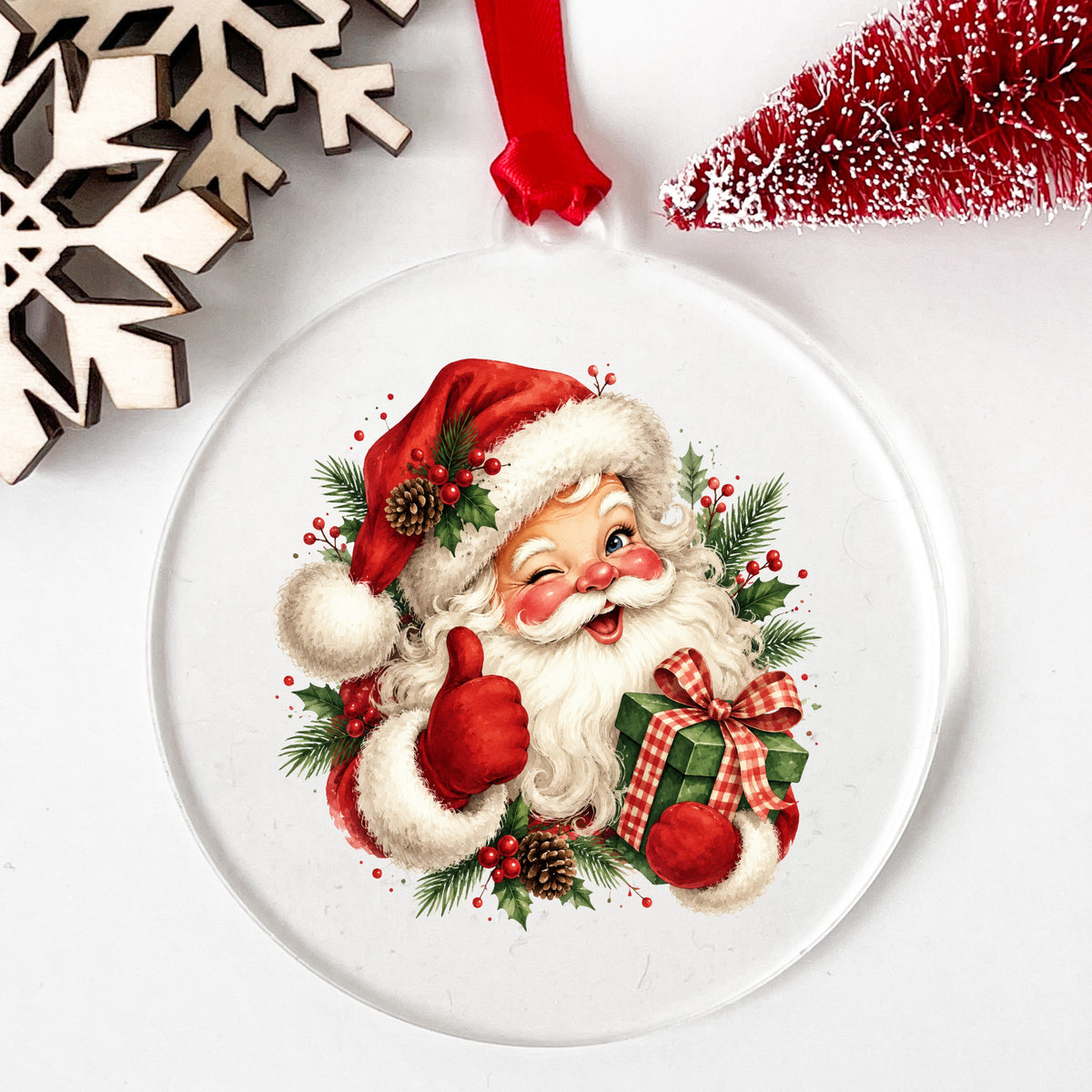 Winking Santa Claus With Gift UV DTF sticker applied to a clear round acrylic ornament with a red ribbon