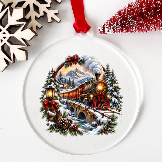 Christmas Train In Snowy Mountains UV DTF sticker applied to a clear round acrylic ornament with a red ribbon