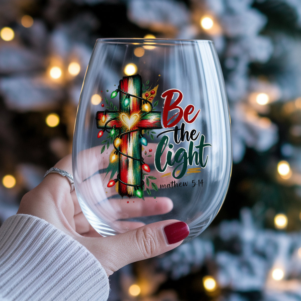 Be The Light Cross With Christmas Lights UV DTF sticker applied to a stemless wine glass held in hand