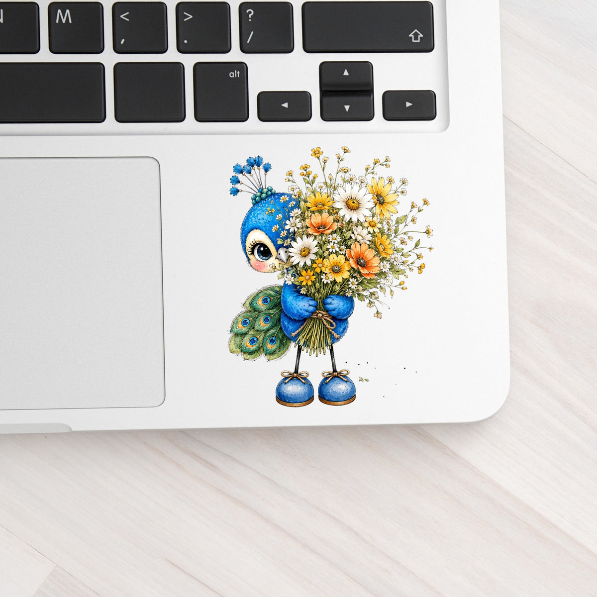 Peacock Holding Wildflower Bouquet UV DTF sticker applied to a silver laptop beside the keyboard