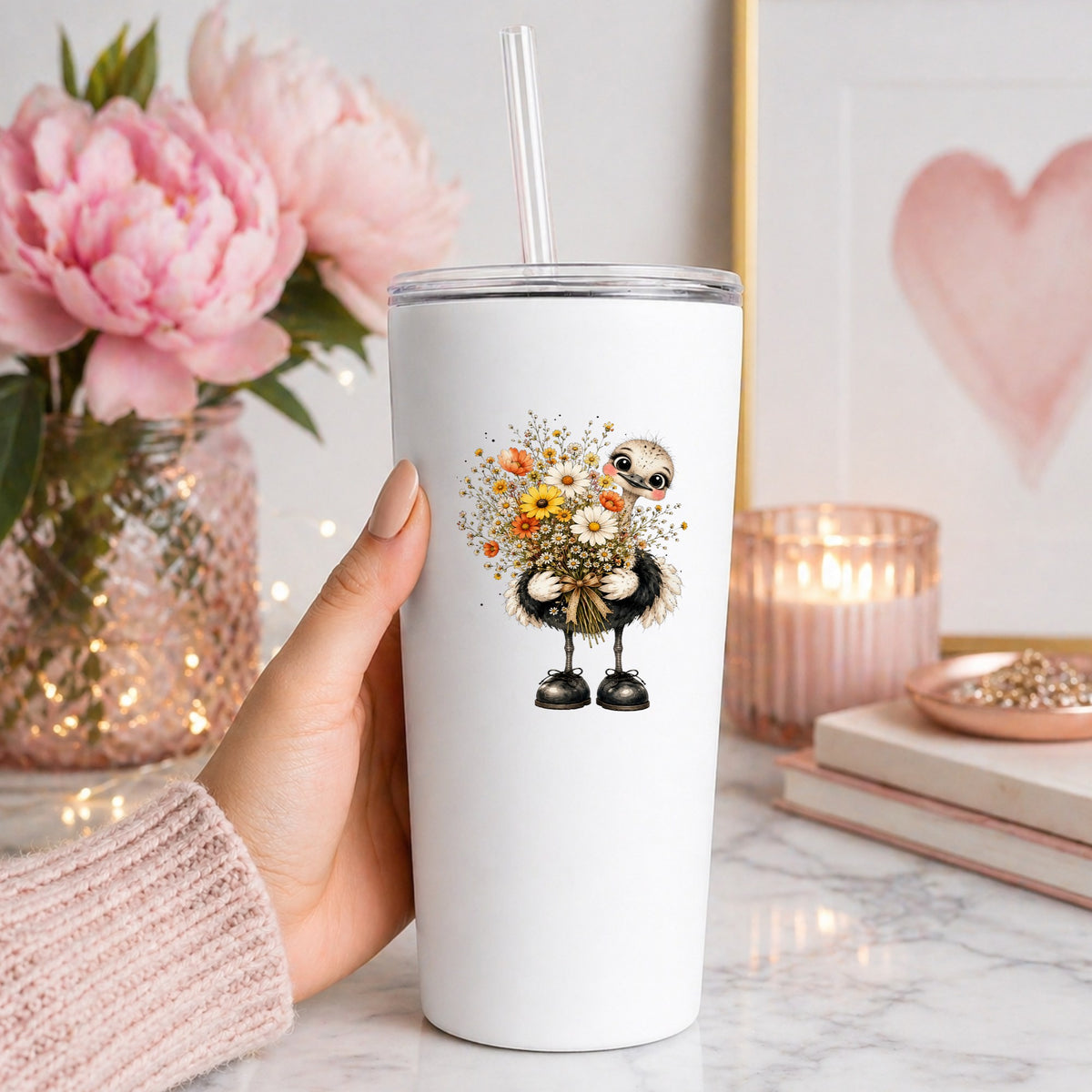 Ostrich Holding Daisy Bouquet UV DTF sticker applied to a white straw tumbler beside pink peonies