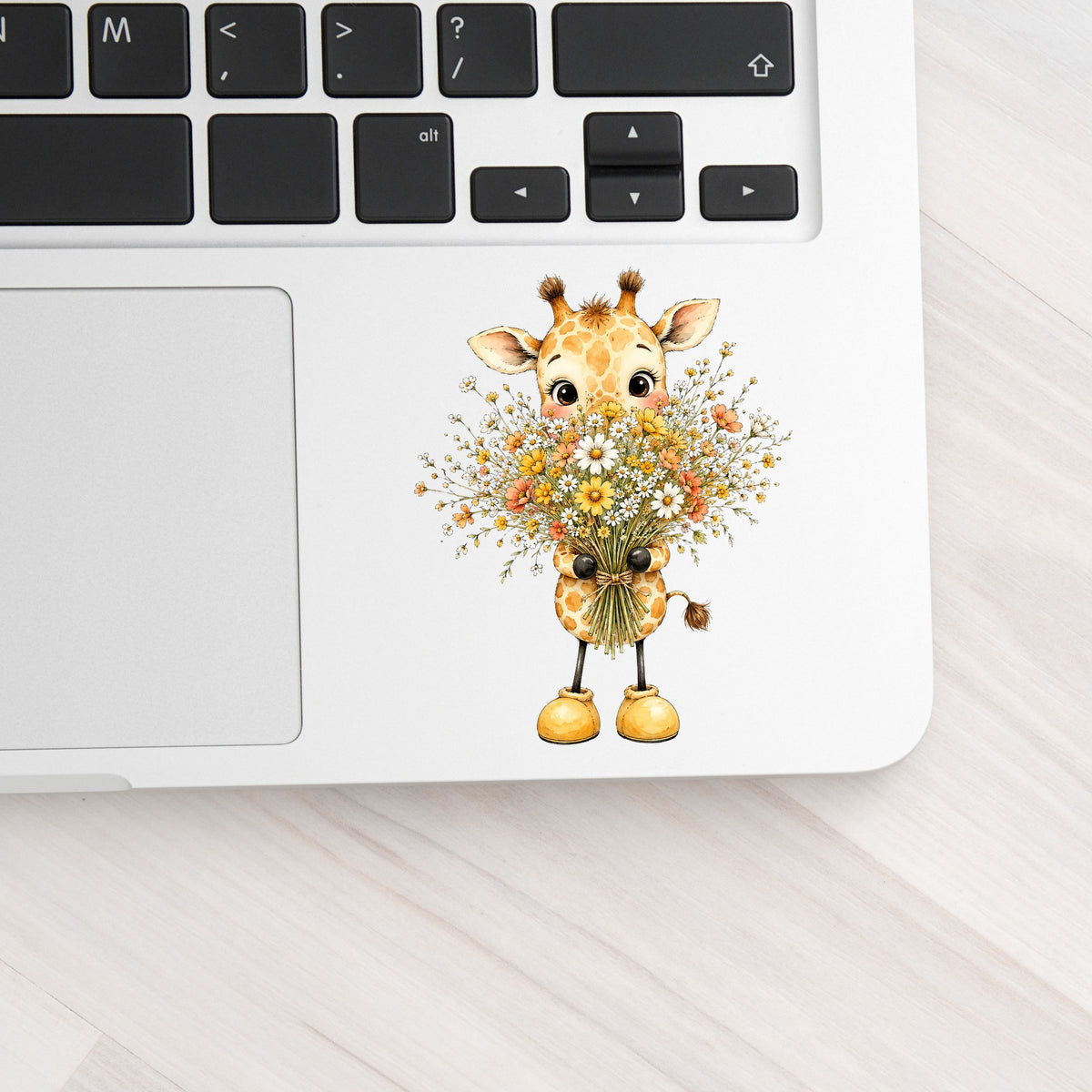 Baby Giraffe Holding Wildflower Bouquet UV DTF sticker applied to a silver laptop beside the keyboard
