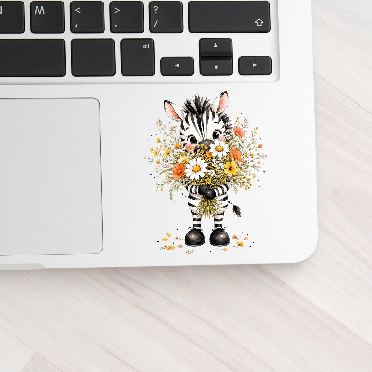 Zebra Holding Wildflower Bouquet UV DTF sticker applied to a silver laptop beside the keyboard