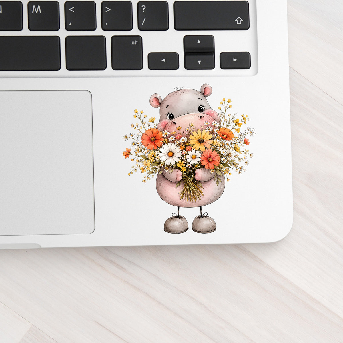 Pink Hippo Holding Wildflower Bouquet UV DTF sticker applied to a silver laptop beside the keyboard