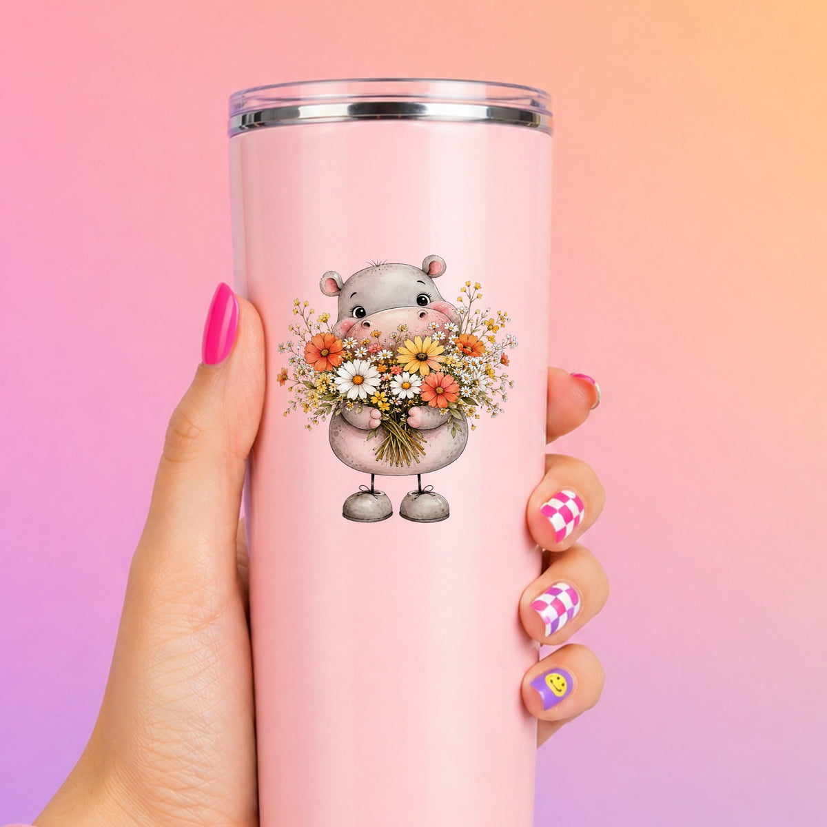 Pink Hippo Holding Wildflower Bouquet UV DTF sticker applied to a tall pink tumbler on a pink and orange background