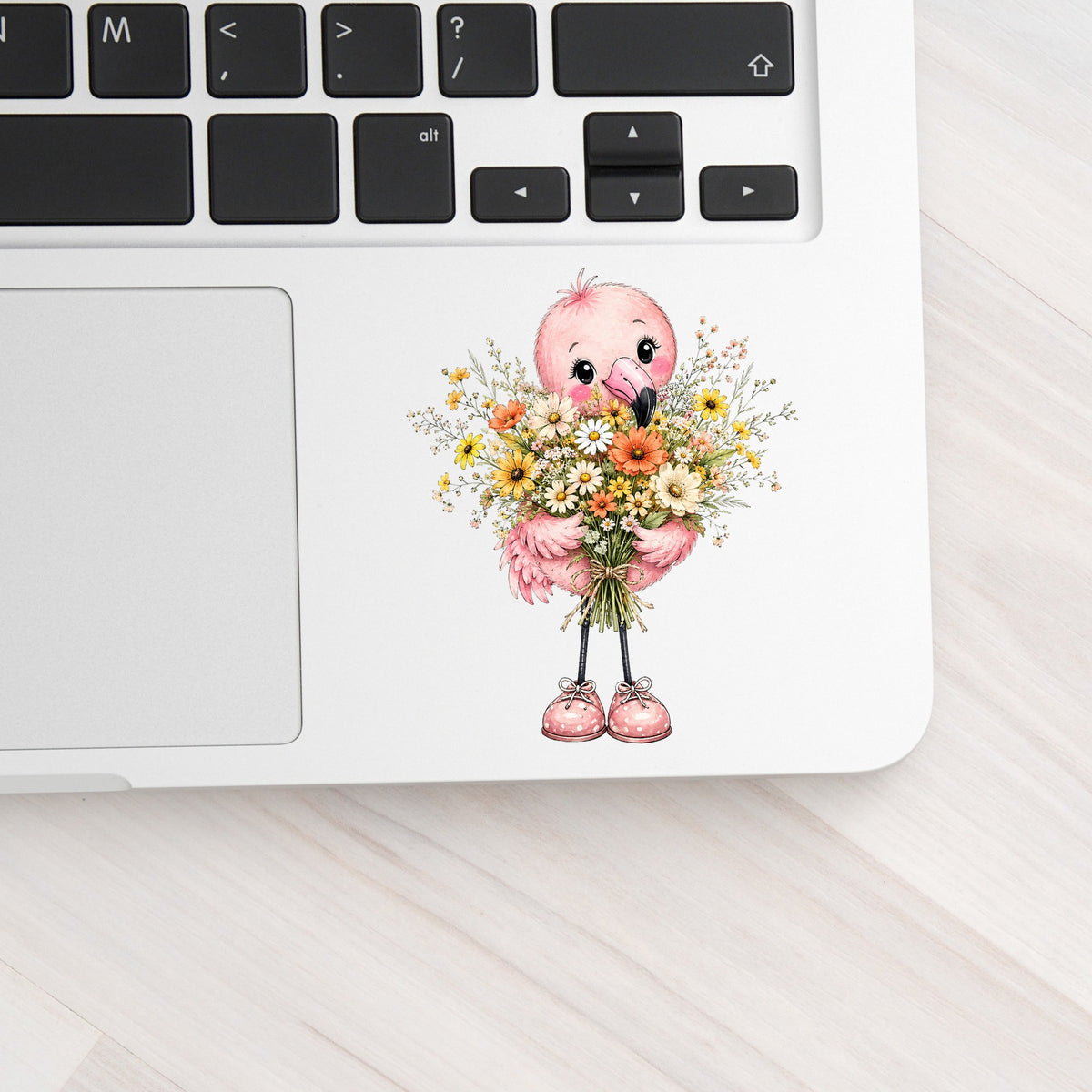 Pink Flamingo Holding Flower Bouquet UV DTF sticker applied to a silver laptop beside the keyboard