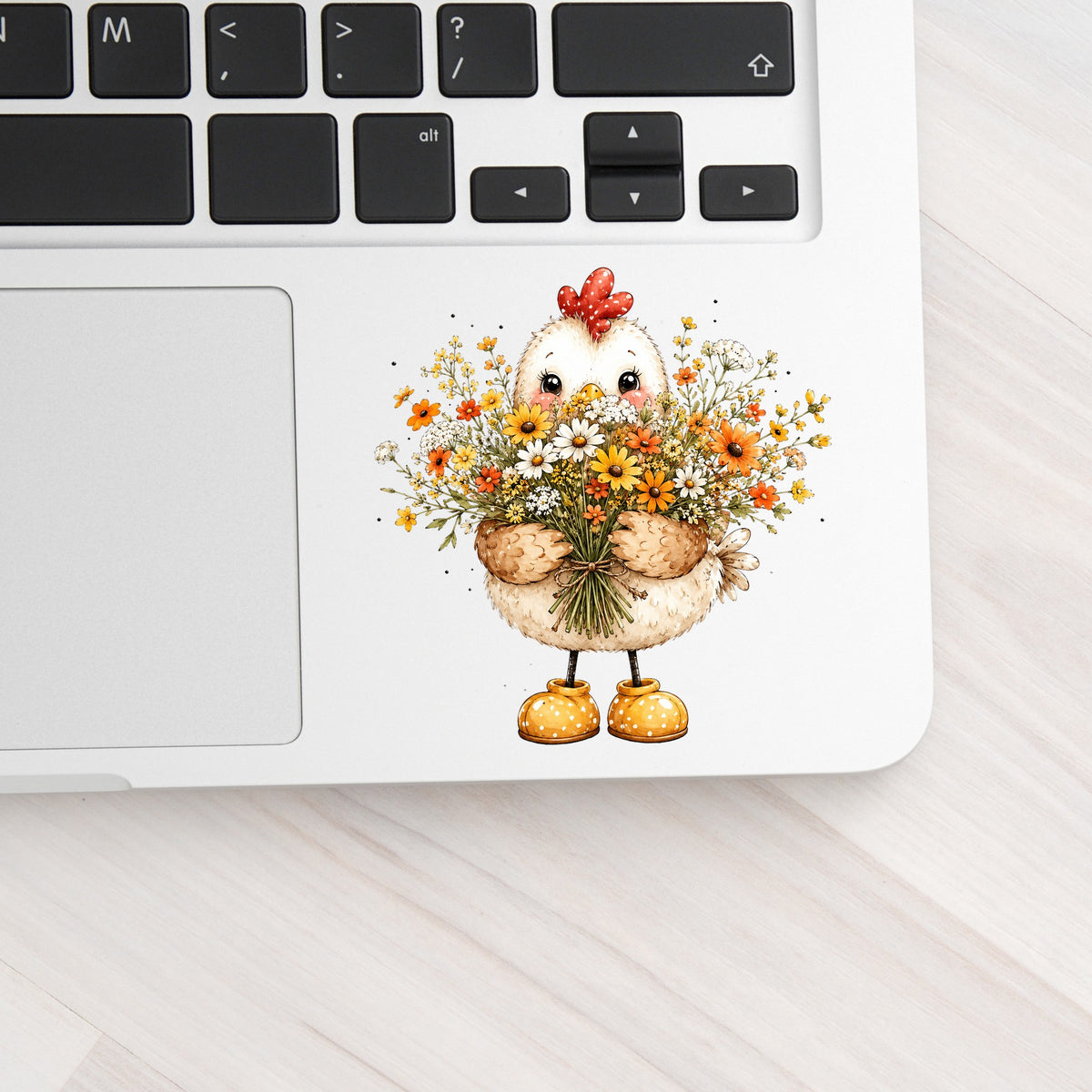 Chicken Holding Wildflower Bouquet UV DTF sticker applied to a silver laptop beside the keyboard