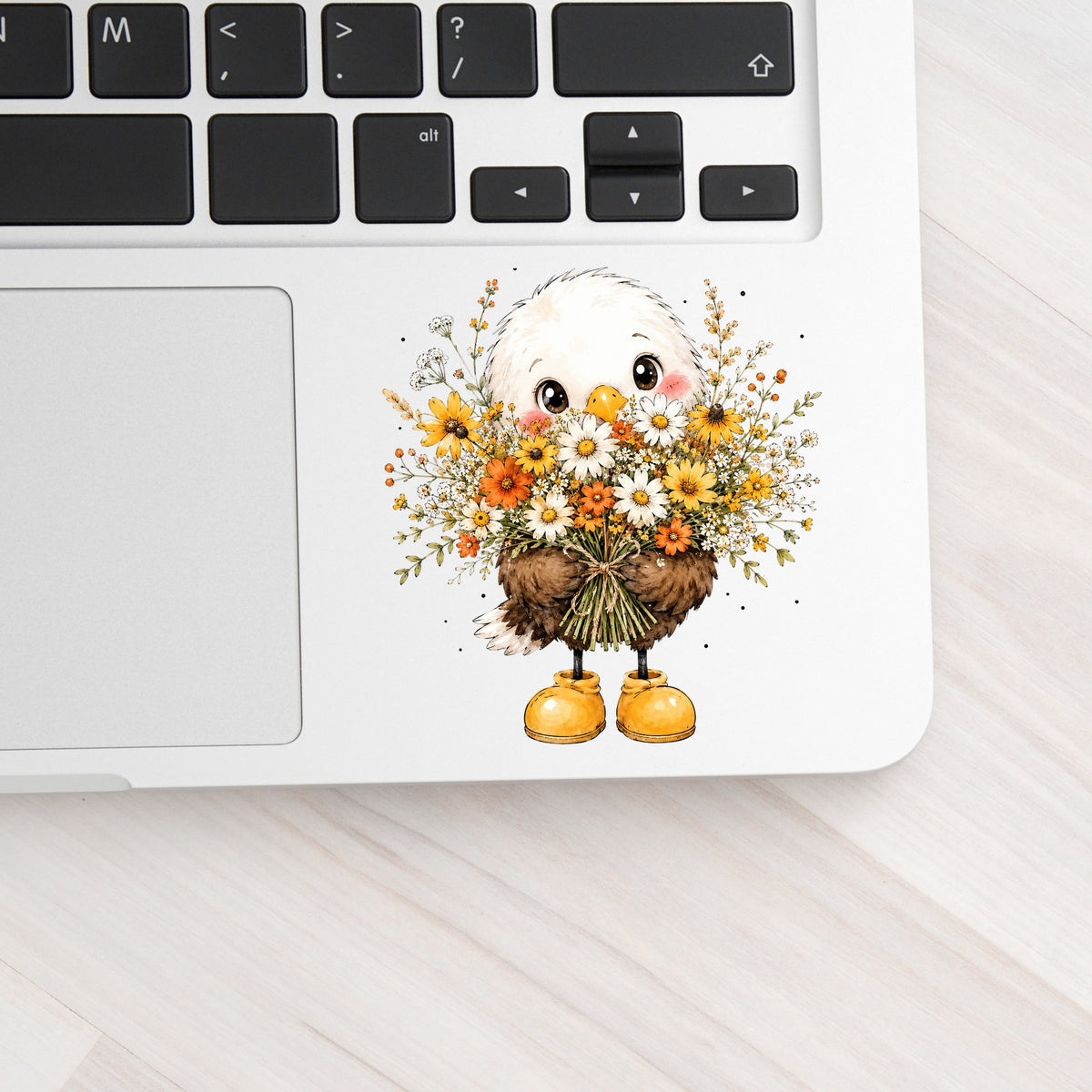 Baby Eagle Holding Daisy Bouquet UV DTF sticker applied to a silver laptop beside the keyboard