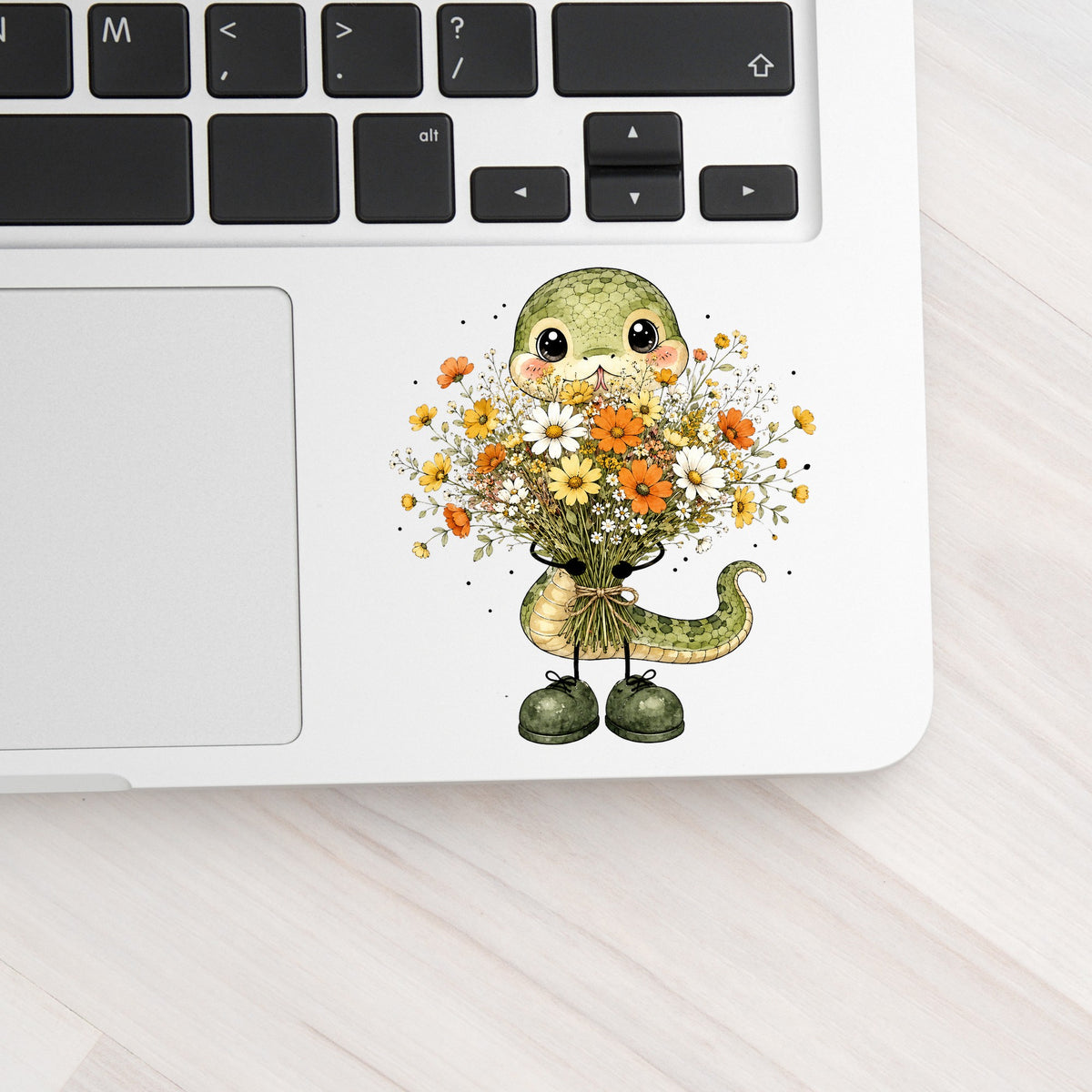 Green Snake Holding Wildflower Bouquet UV DTF sticker applied to a silver laptop beside the keyboard