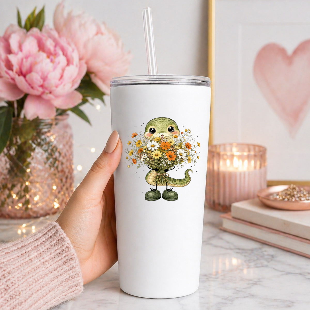 Green Snake Holding Wildflower Bouquet UV DTF sticker applied to a white straw tumbler beside pink peonies