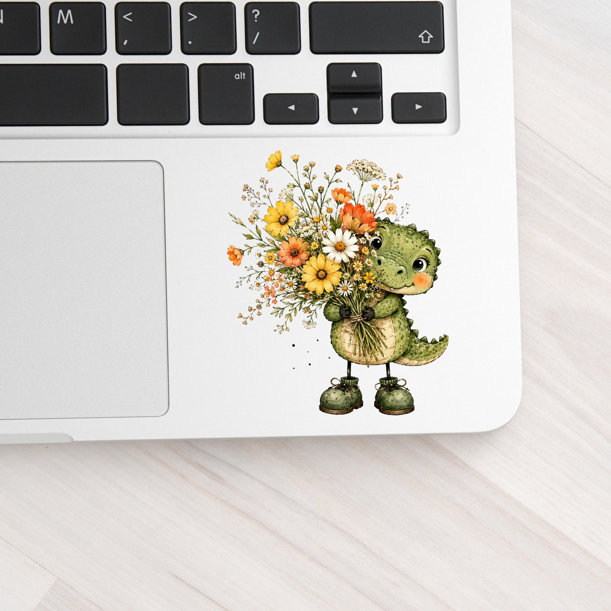 Baby Crocodile Holding Flower Bouquet UV DTF sticker applied to a silver laptop beside the keyboard