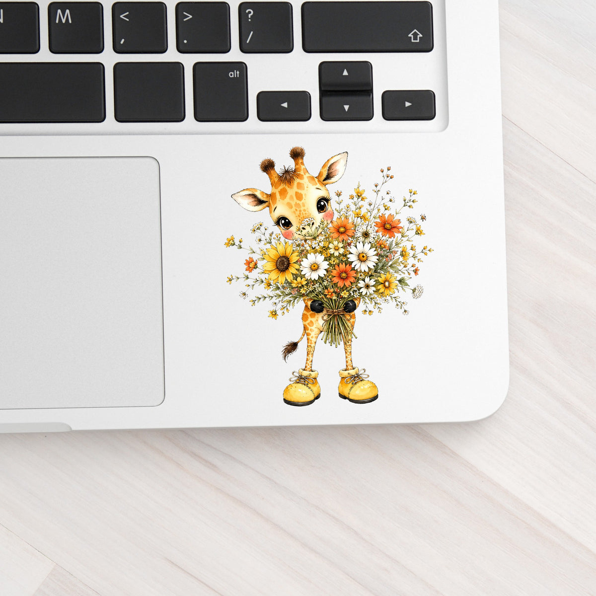 Giraffe Holding Sunflower Bouquet UV DTF sticker applied to a silver laptop beside the keyboard