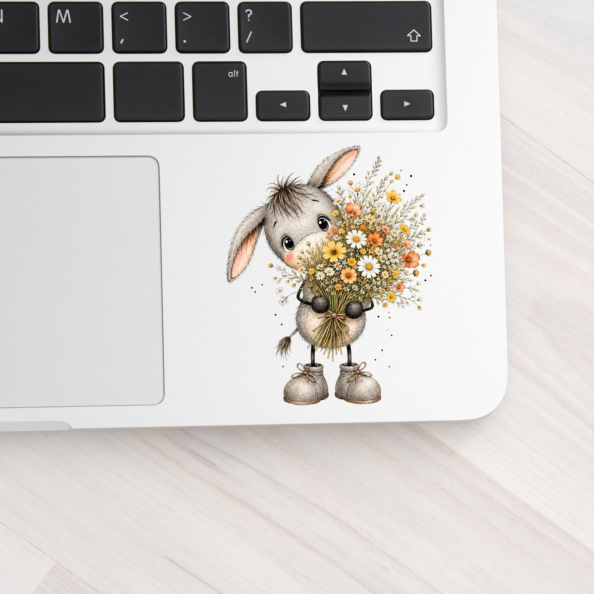 Baby Donkey Holding Wildflower Bouquet UV DTF sticker applied to a silver laptop beside the keyboard