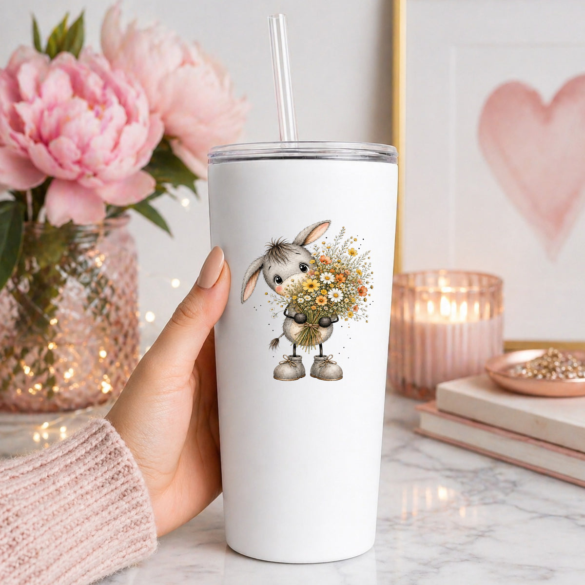 Baby Donkey Holding Wildflower Bouquet UV DTF sticker applied to a white straw tumbler beside pink peonies