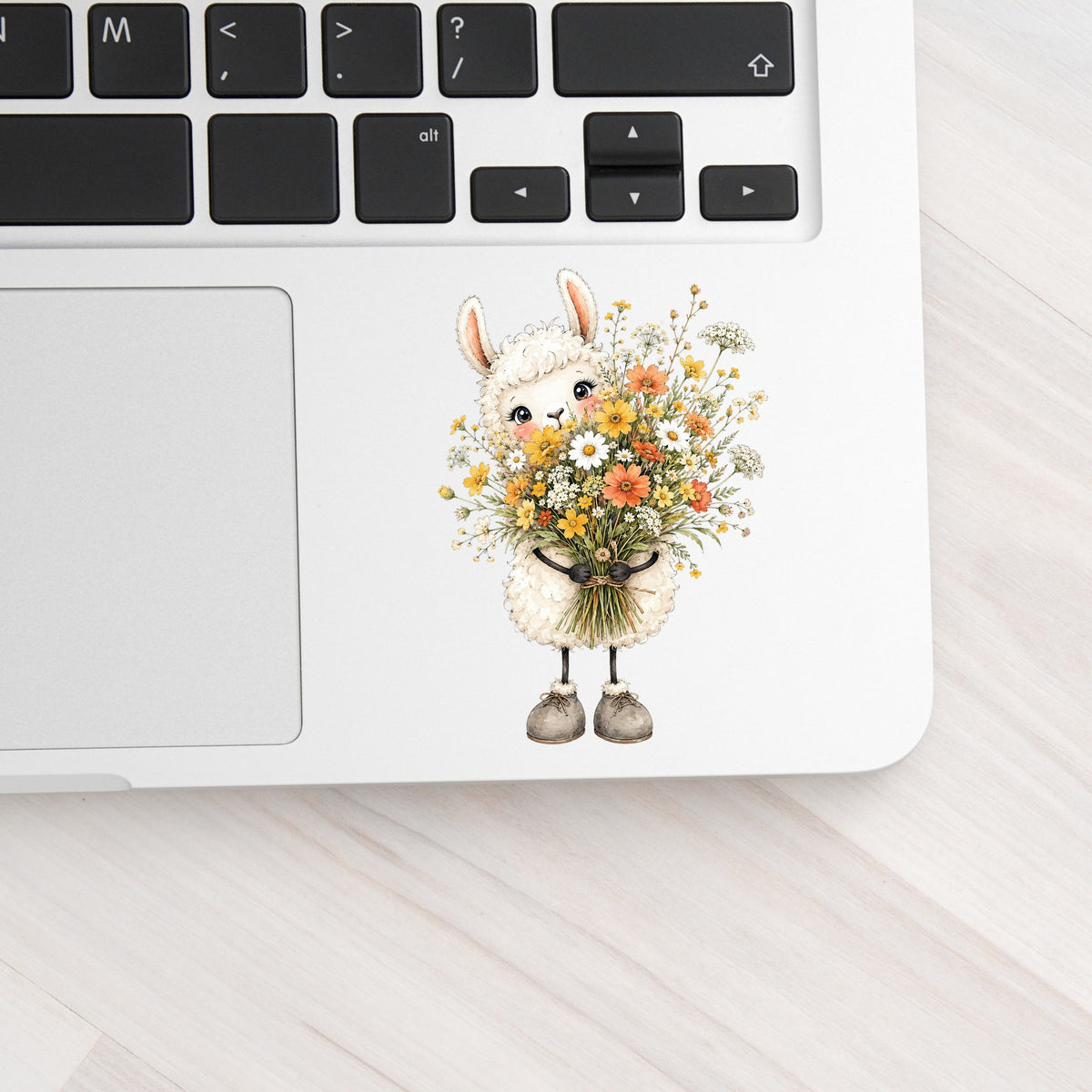 White Llama Holding Daisy Bouquet UV DTF sticker applied to a silver laptop beside the keyboard