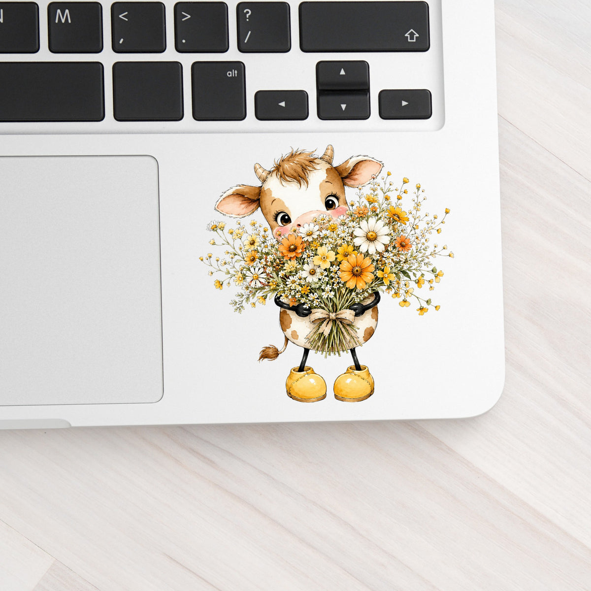 Baby Cow Holding Wildflower Bouquet UV DTF sticker applied to a silver laptop beside the keyboard