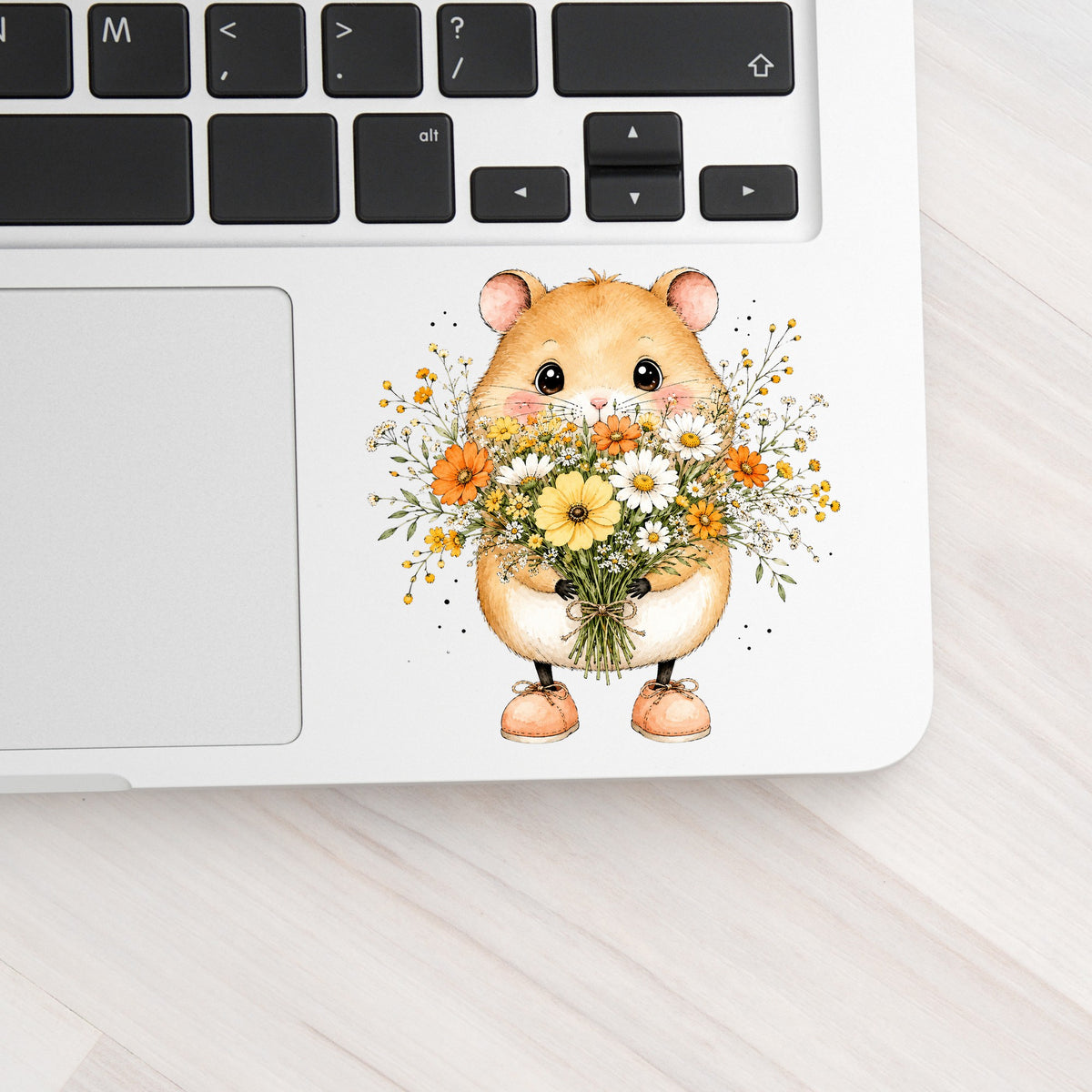 Hamster Holding Wildflower Bouquet UV DTF sticker applied to a silver laptop beside the keyboard