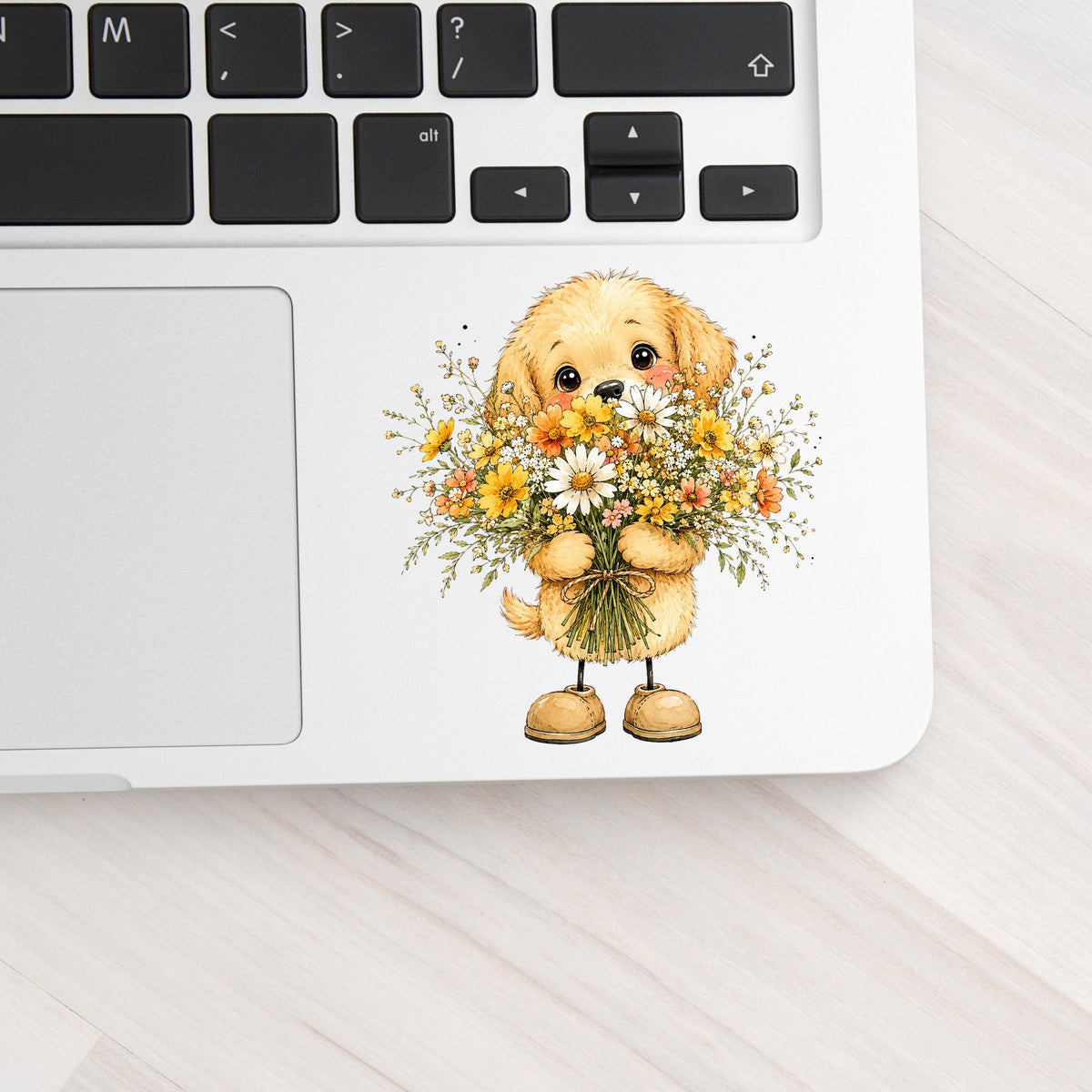 Golden Puppy Holding Daisy Bouquet UV DTF sticker applied to a silver laptop beside the keyboard