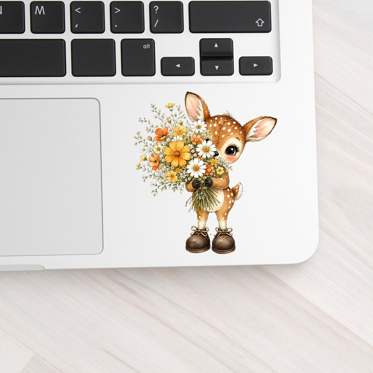 Baby Deer Holding Wildflower Bouquet UV DTF sticker applied to a silver laptop beside the keyboard