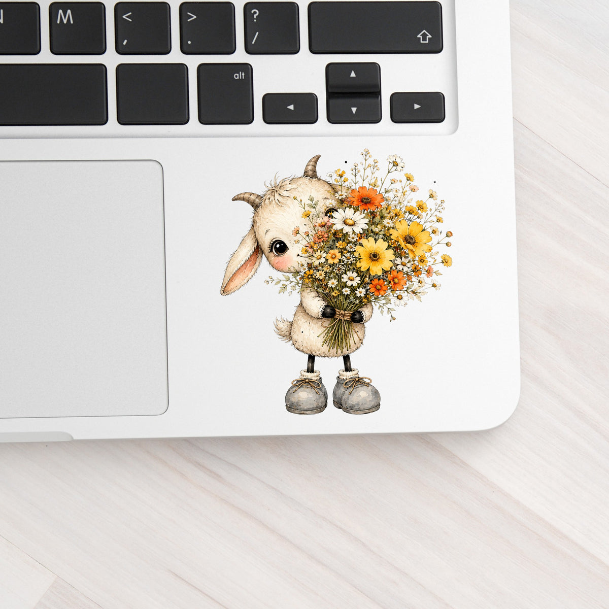 Baby Goat Holding Wildflower Bouquet UV DTF sticker applied to a silver laptop beside the keyboard