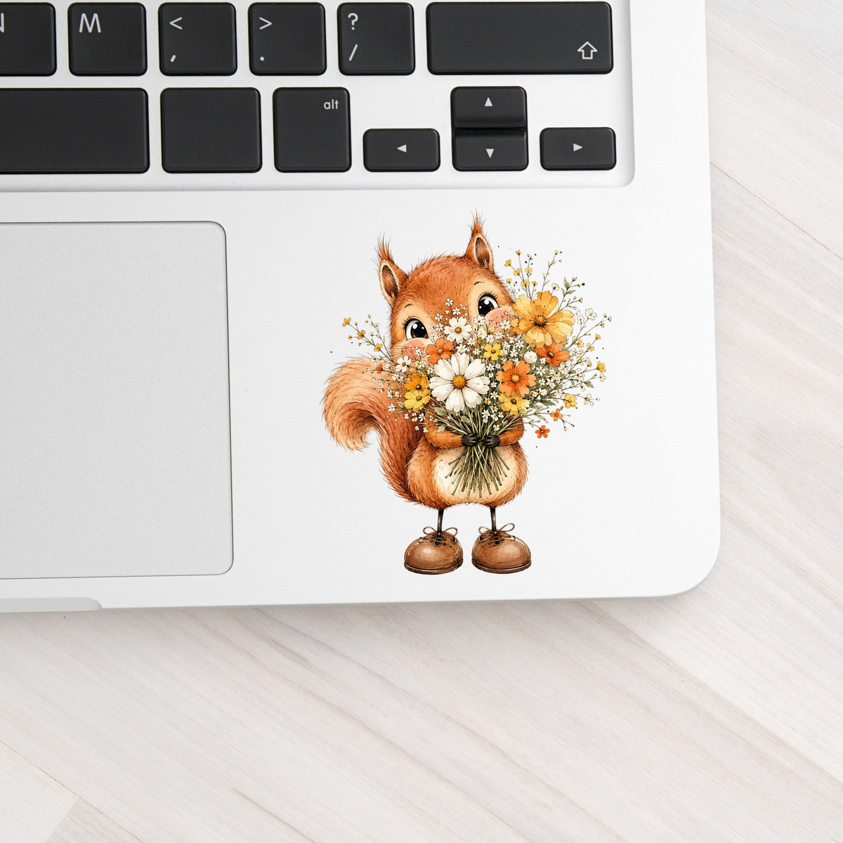 Red Squirrel Holding Daisy Bouquet UV DTF sticker applied to a silver laptop beside the keyboard