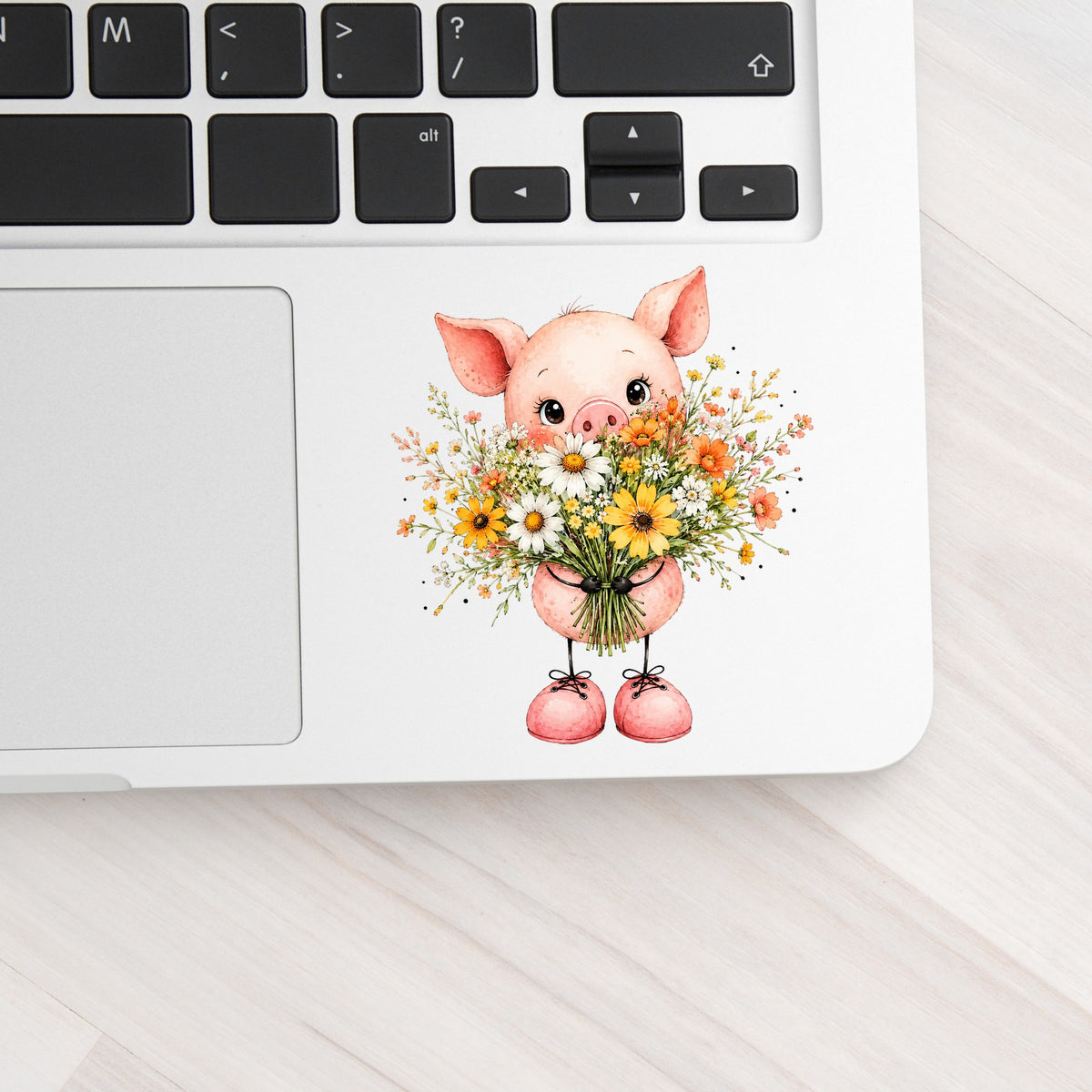 Baby Pig Holding Daisy Bouquet UV DTF sticker applied to a silver laptop beside the keyboard