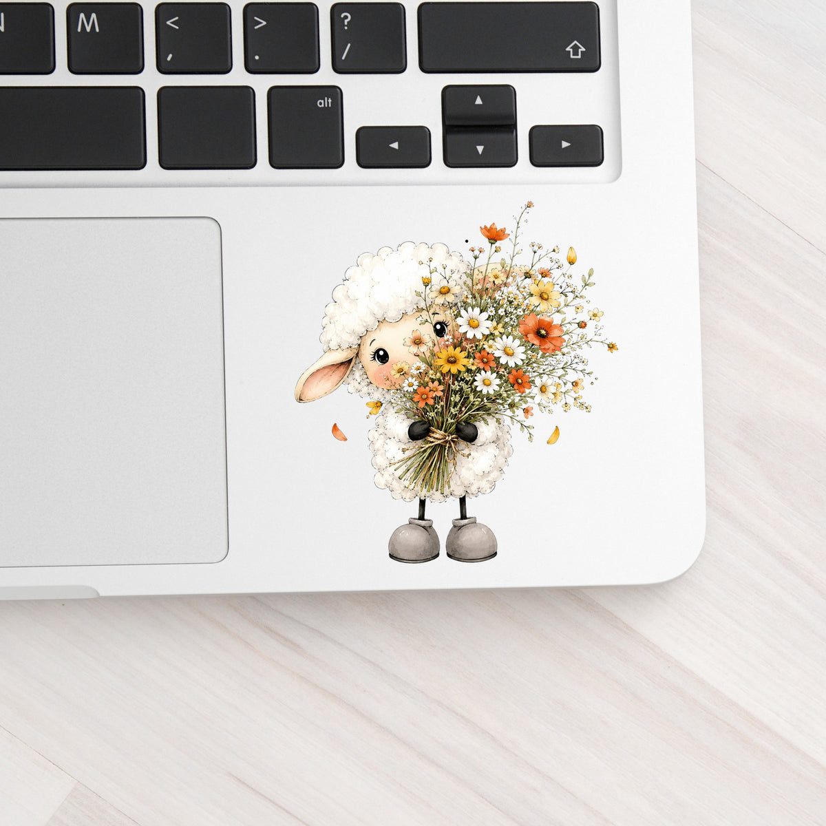 White Lamb Holding Wildflower Bouquet UV DTF sticker applied to a silver laptop beside the keyboard