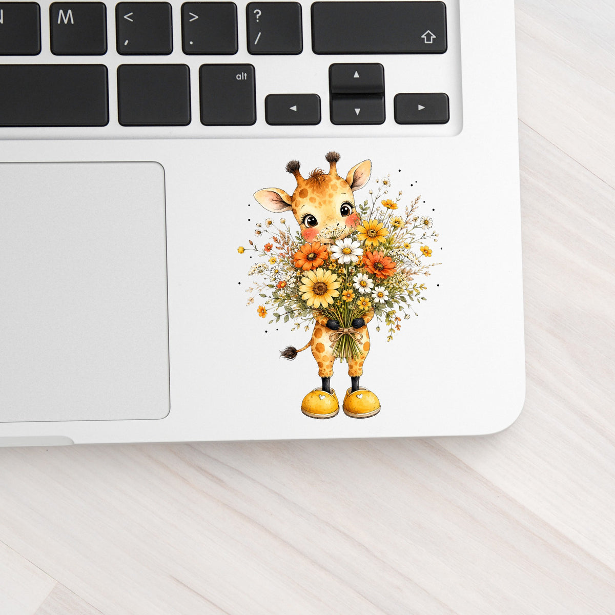 Watercolor Giraffe Holding Daisy Bouquet UV DTF sticker applied to a silver laptop beside the keyboard