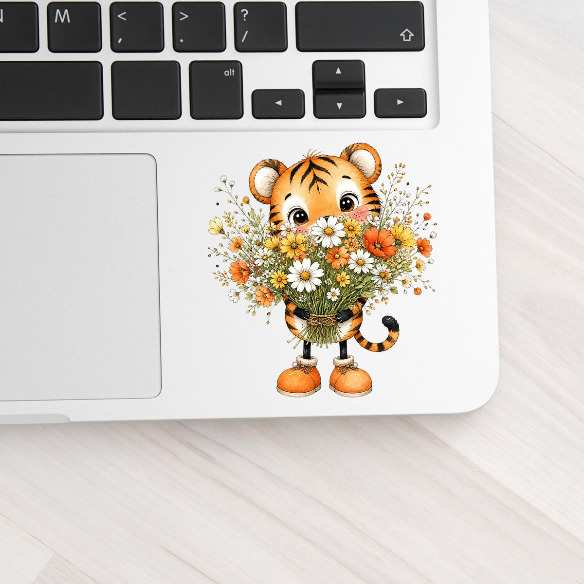Tiger Cub Holding Wildflower Bouquet UV DTF sticker applied to a silver laptop beside the keyboard